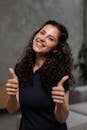 Cheerful woman with curly hair giving thumbs up indoors, smiling brightly.